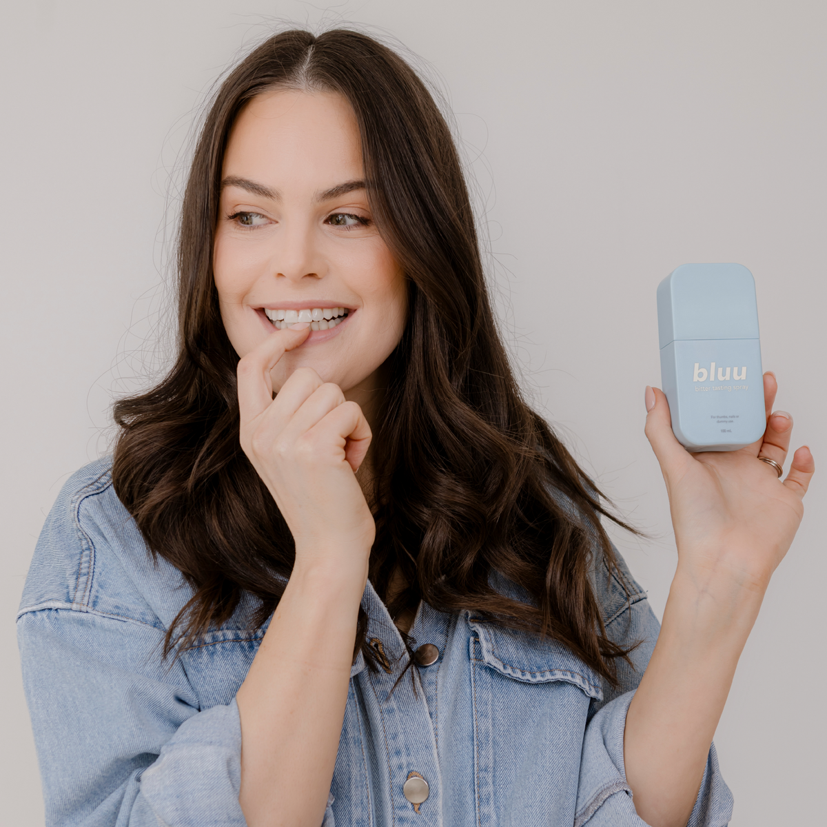 Woman biting her nail while holding Bluu bitter tasting spray, used to help adults stop nail biting from stress